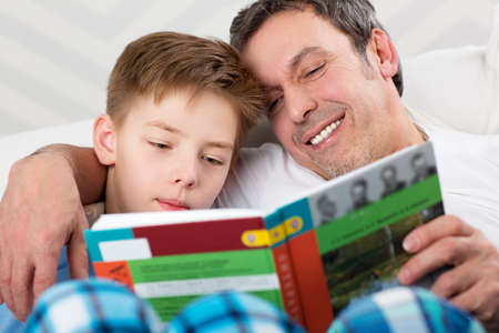Father and son reading a book. Careful dad helping child to learn new things