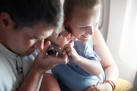 Mother father and little son in the airplane. The have handsfree talking on the cell or listening somethingの写真素材
