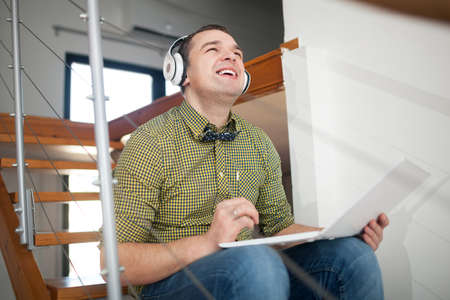 Happy hipster style man listening to music in wireless earphones and using laptop while sitting on...