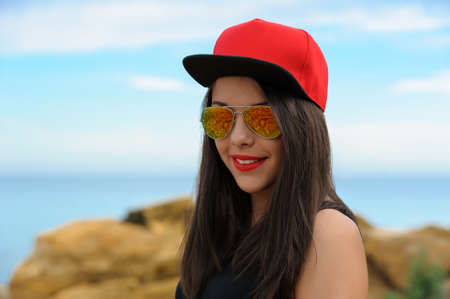 Young beautiful smiling brunette girl in red cap and sun glasses against blue skyの写真素材