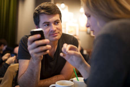 Young man using cellphone during the meeting with a girl in a cafe, but his look is attracted by...