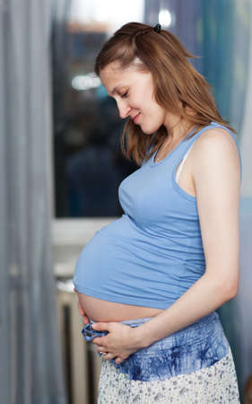 Pregnant woman stands in the room with her hands on belly