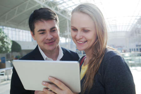 Young man and woman in shopping centre watching something on tablet PC with happy lookの写真素材