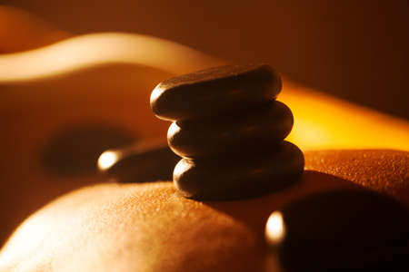 Close-up shot of woman receiving hot stone massage at beauty spa. Black rocks on the skin shining in sunlightの写真素材
