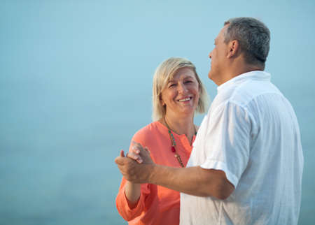 Happy middle-aged couple wearing casual summer clothes while dancing outdoors on a romantic song