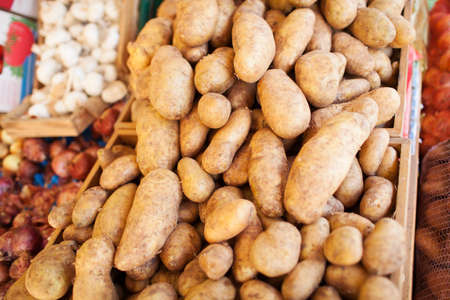Close Up of Brown Russet Baking Potatoes Piled in Crates at Food Market with Other Produce in Backgroundの写真素材