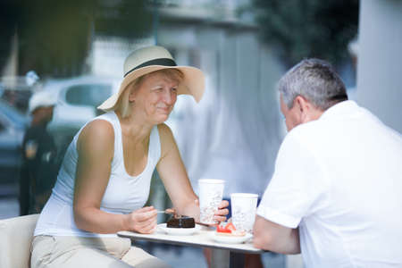 Happy woman in hat eating in outdoor cafe with her husbandの写真素材