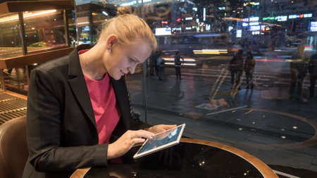 Young woman using tablet computer in the cafe in the evening, people and traffic in the street outside. Seoul, South Koreaの写真素材