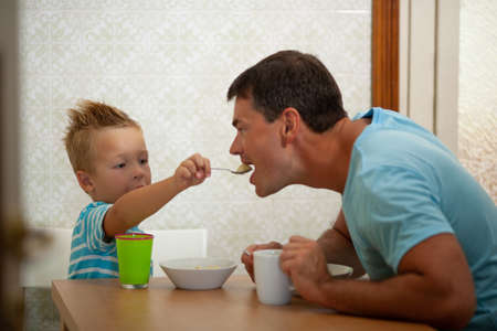 A boy spoon-feeds his father with porridgeの写真素材