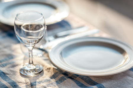 A fragment of a laid table with a tablecloth, a couple of plates, glasses and cutleryの写真素材