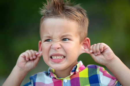 A little boy, making a scaring grimace, pulling his ears aside