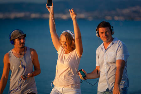 Group of three young people feeling free, enjoying life and excited with music. Woman and two men...