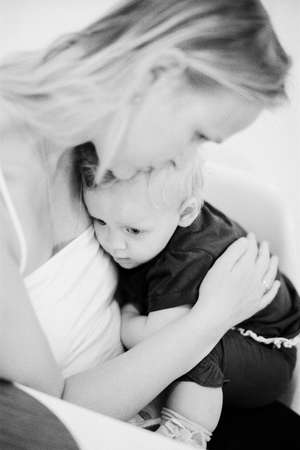 Black and white shot of mother embracing one year old daughter sitting on her lap. Child cuddling mum to feel love, safety and careの写真素材