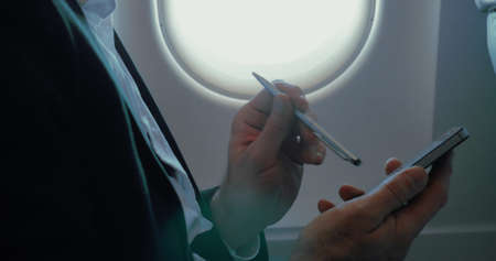 Close-up shot of a businessman using pen to type on smartphone in the plane. Communication during the flightの写真素材