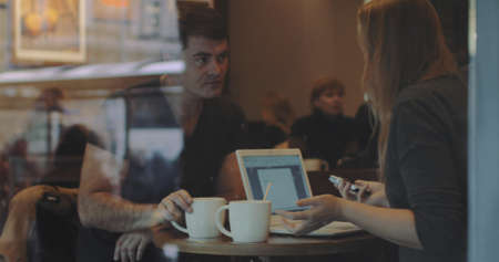 Two fiends are sitting in cafe and have lively conversation, woman is holding a smartphone and...