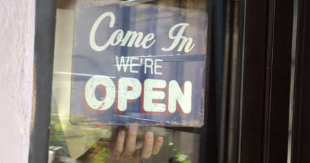 Dolly shot of woman closing the glass door and turning over vintage style shop-sign from open to...