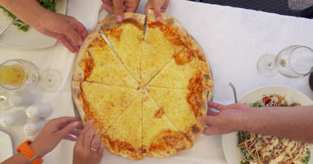 People taking slices of cheese pizza served in cafeの写真素材
