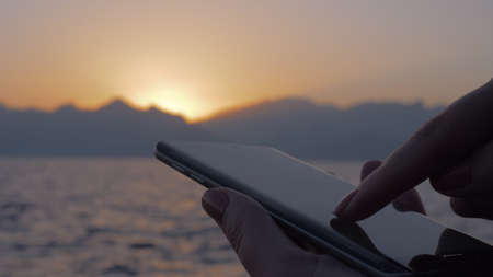 Woman using cellphone on sea and sunset backgroundの写真素材