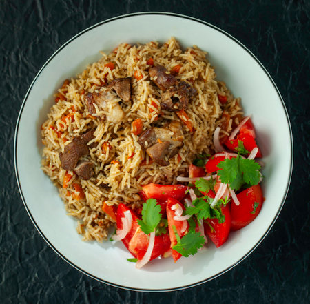 Delicious pilaf dish made with lamb, rice, and spices, accompanied by a refreshing tomato and onion salad with cilantroの写真素材