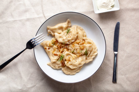 Plate of potato and cheese pierogies is served with fried onions and fresh dill, making a delicious...