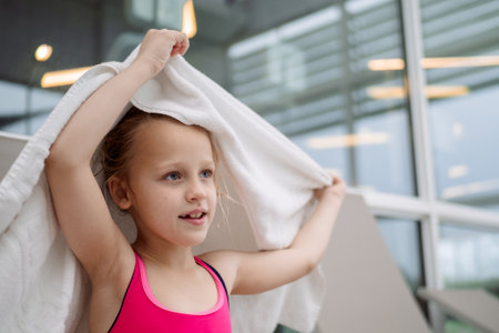 Caucasian girl in a pink swimsuit drying her hair with a white towel in an indoor pool areaの写真素材