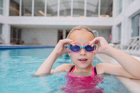 Caucasian girl wearing pink swimwear adjusting blue goggles in an indoor swimming poolの写真素材