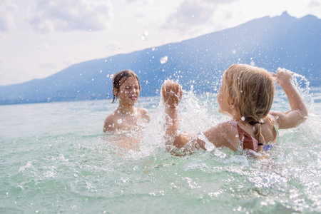 Children having fun splashing water while playing in a calm lake with scenic mountainsの写真素材