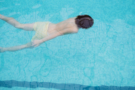 Teenager swimming underwater in a clear blue indoor swimming pool filmed from aboveの写真素材