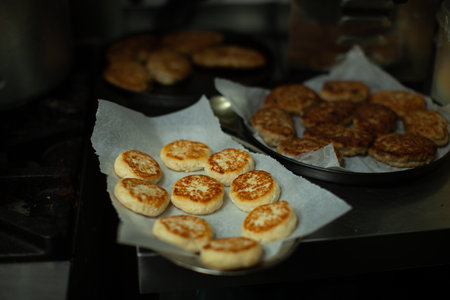 Delicious golden brown syrniki cooling on baking paper after being cooked, with other food items in the background in a professional kitchen settingの写真素材