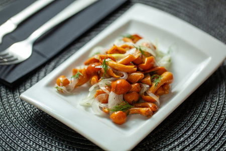 Close-up of marinated mushrooms garnished with onion and dill on a white plate with cutleryの写真素材