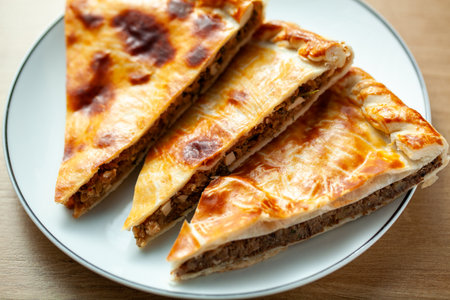 Three slices of traditional Russian meat pies served on a white plate The pies have a golden brown...