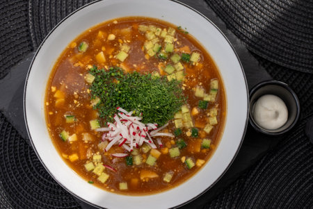 Okroshka, a traditional Russian cold soup made with kvass, features diced vegetables like potatoes, cucumbers, and radishes, garnished with fresh herbs and sour creamの写真素材