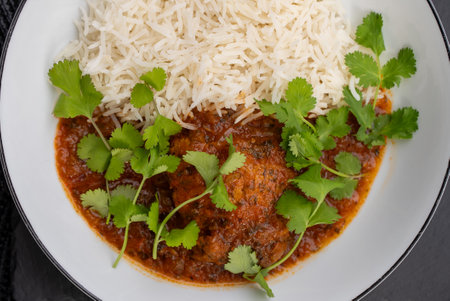 Chicken tikka masala served with basmati rice and garnished with fresh coriander leaves, shot from above in a white bowl, offering a vibrant and appetizing presentation of a classic Indian dishの写真素材