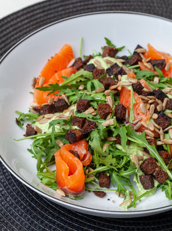 Fresh and healthy salmon salad with arugula, crispy croutons, sunflower seeds and creamy pesto dressing, served in a stylish white bowlの写真素材