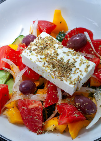 Fresh and vibrant Greek salad featuring a generous slab of feta cheese sprinkled with oregano, Kalamata olives, juicy tomatoes, crisp cucumbers, crunchy onions, and colorful bell peppersの写真素材