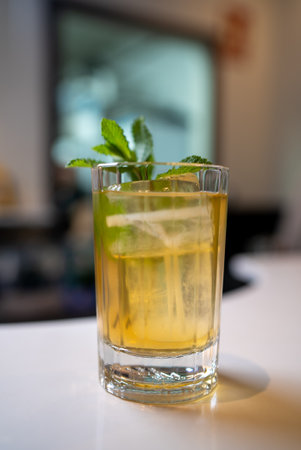 Tall crystal glass filled with refreshing iced tea, ice cubes, and garnished with a sprig of fresh mint, sits on a white surface, creating a cool and inviting summer beverageの写真素材