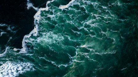 Aerial view of dark green ocean water with white splashes and foam, creating a beautiful abstract...