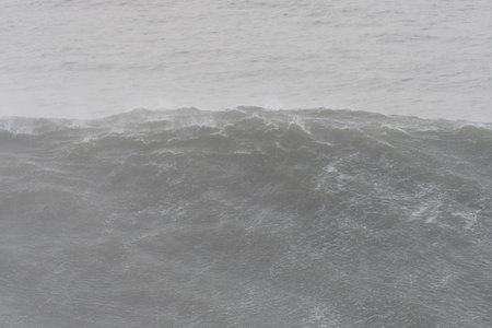 Dramatic ocean wave crashing against rocky shores on a stormy day, generating powerful white foam...