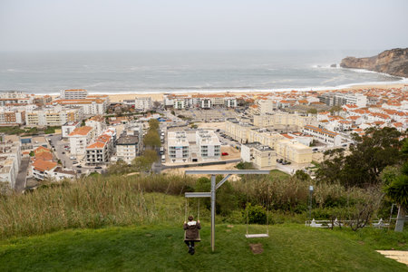 Tourist swinging on a hilltop viewpoint overlooking the town of Nazare and its beach in Portugal