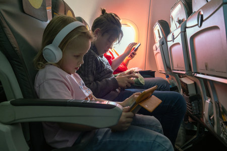 Young passengers using smartphones and tablets during a flight, enjoying entertainment and...