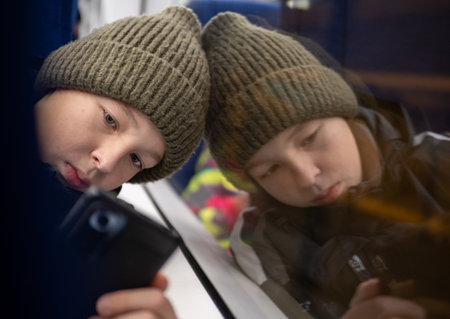 Boy traveling by train, engrossed in their smartphone, create a captivating reflection in the window...