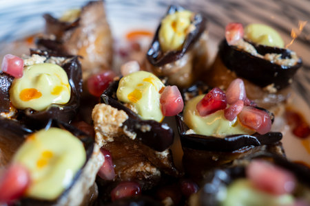 Eggplant rolls featuring pomegranate seeds and smooth white sauce, presenting elegant Mediterranean...