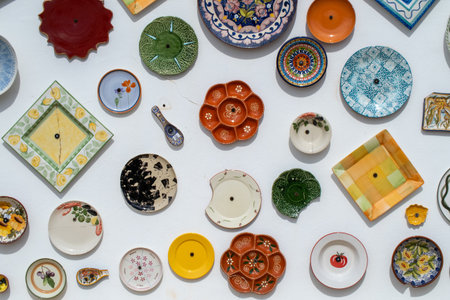 Traditional ceramic plates and spoons with various shapes, colors and decorations hanging on a white wall, creating a vibrant and artistic displayの写真素材