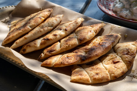 Slices of pita bread seasoned with honey and oregano are arranged on a wooden tray covered with baking paper, ready to be servedの写真素材