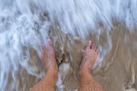 Gentle waves caressing sandy beach, bare feet embracing oceans edge, sunlight warming travelers skin during peaceful seaside momentの写真素材