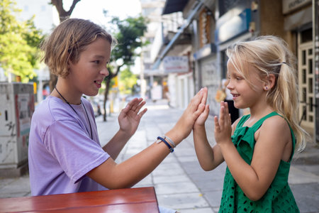 Two joyful siblings playing patty cake at an outdoor cafe table, sharing laughter and creating cherished memories during a sunny summer dayの写真素材