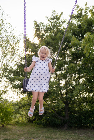 Happy child swinging joyfully on a swing in a park, relishing summer holidays and embracing playful...