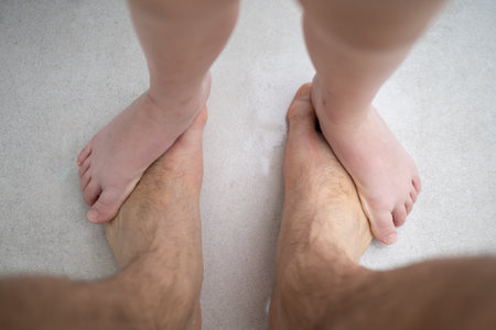 Small childs bare feet standing on top of large adult mans bare feet on white carpet, representing family bond and playful interactionの写真素材