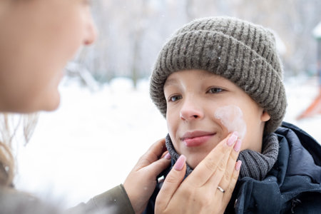 Caring mother applying protective sunscreen or moisturizing cream on her sons face during wintertime outdoor activitiesの写真素材