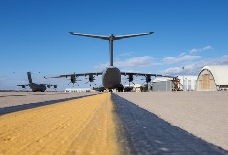 Large military transport aircraft with four turboprop engines parked on runway near hangars under...